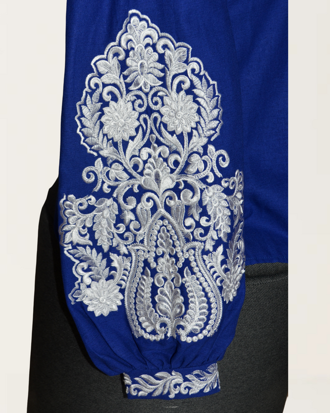 Blue blouse featuring intricate white floral embroidery on the sleeve, showcasing elegant design elements.