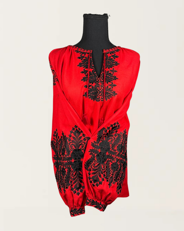 Red blouse with intricate black embroidery displayed on a mannequin against a neutral background.